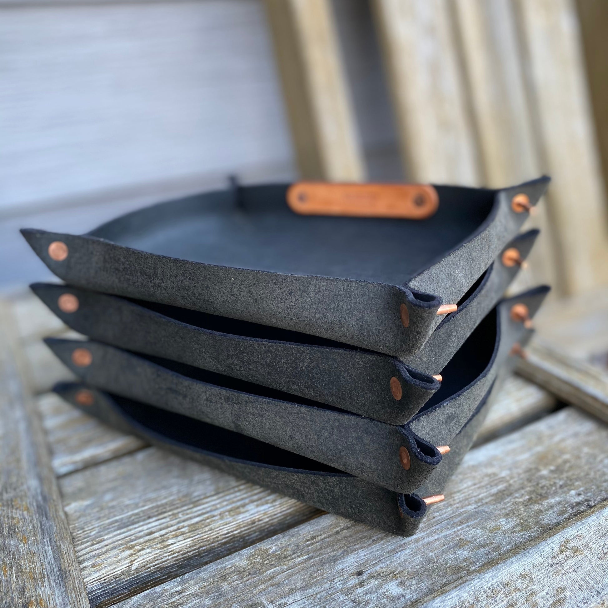 Stack of black leather valet trays with brown handles on a wooden surface
