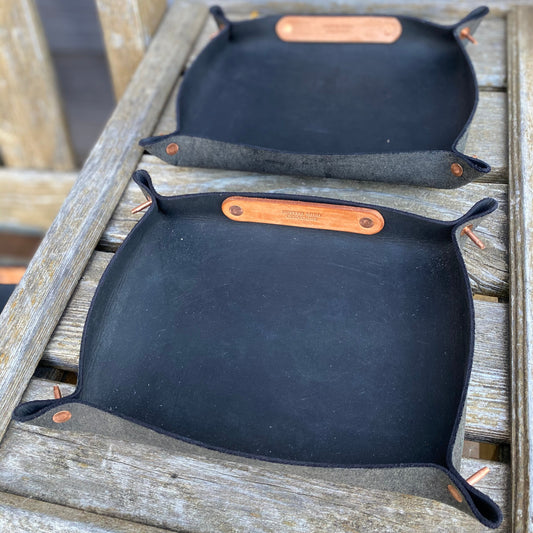Two black leather valet trays with brown leather straps on a wooden surface