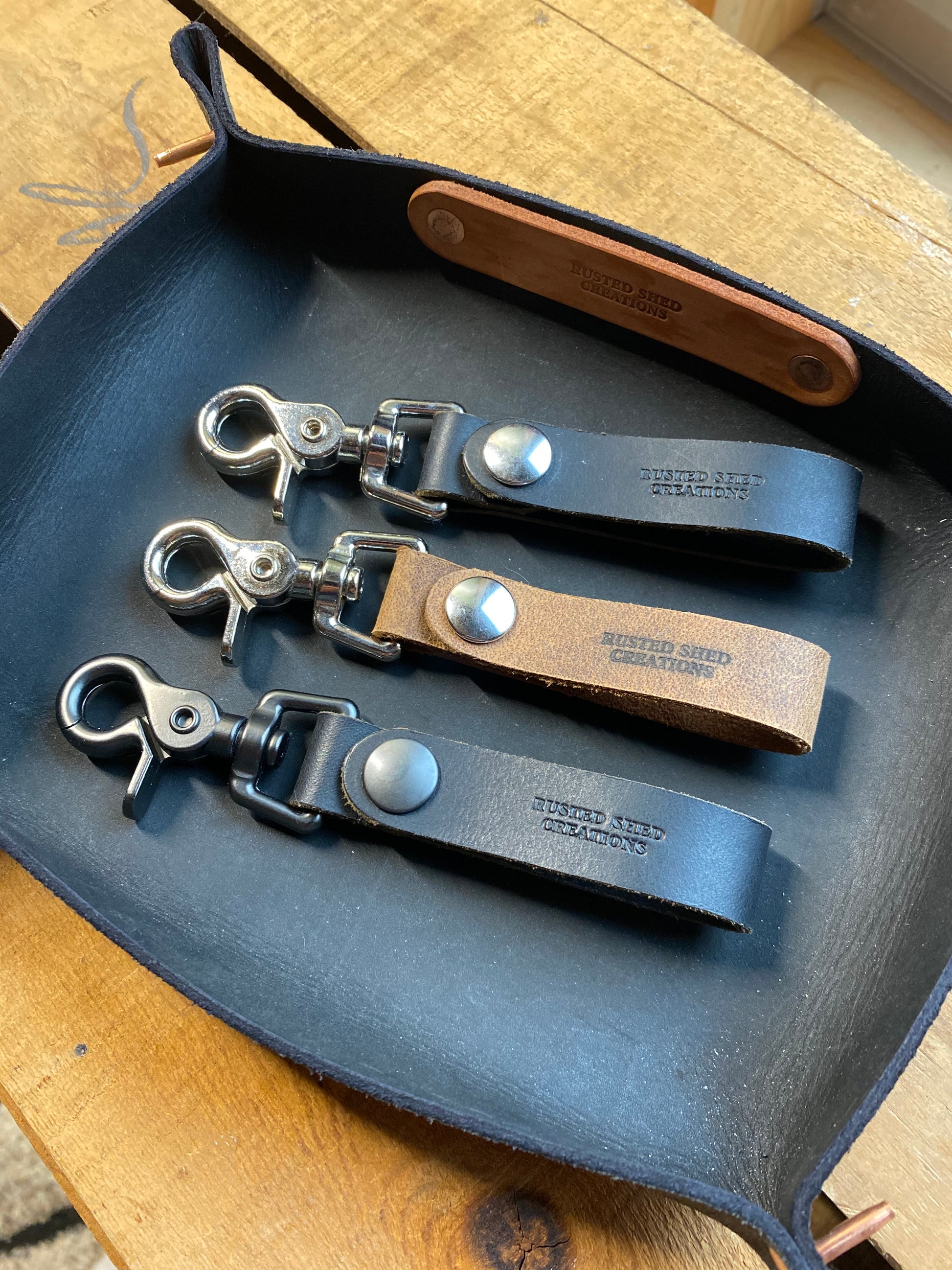 Three leather keychains with metal clasps on a leather valet tray